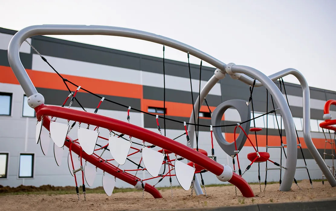 A shark-themed climbing structure with rope nets and curved frames, featuring tooth-like panels along a red beam.