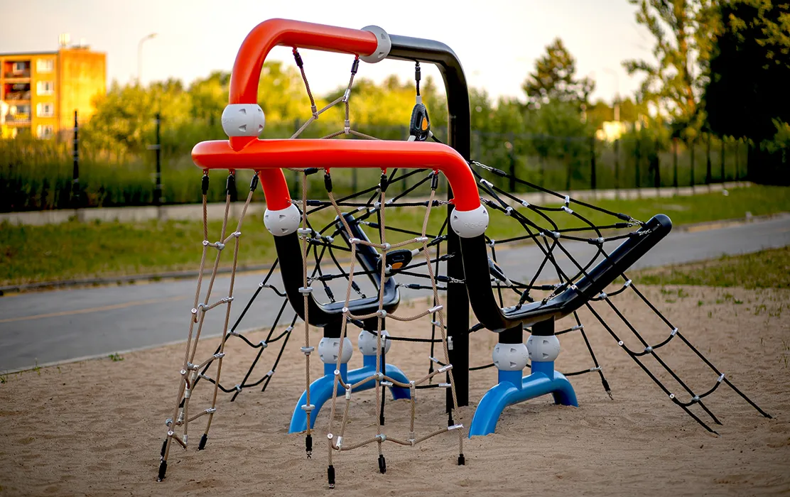 A toucan-themed play structure with rope climbing nets and colorful curved frames set in a sandy play area.