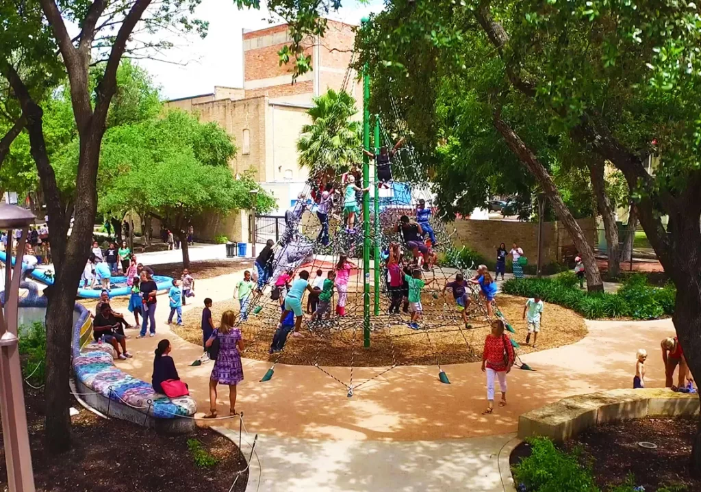 Busy playground with kids climbing large rope pyramid and shaded seating area