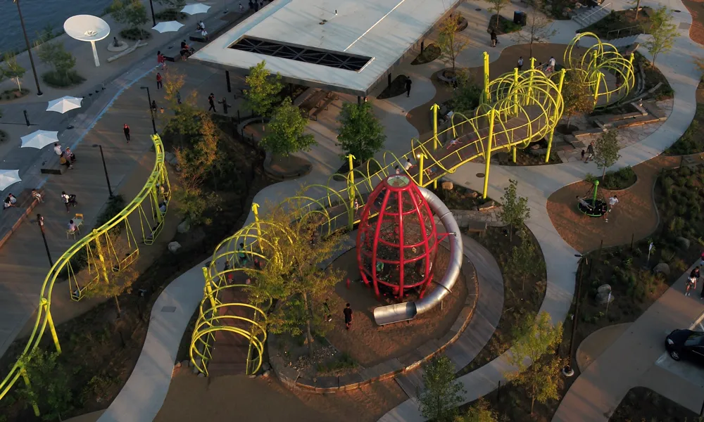 Overhead view of a landscaped park with curving walkways, a red climbing structure, and green spiral bridges.