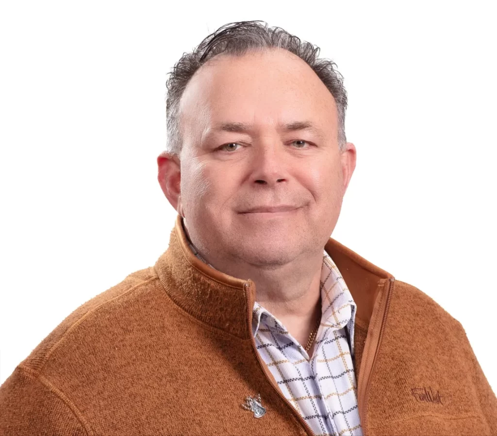 Portrait of a man in a brown zip-up jacket over a patterned shirt, facing forward.