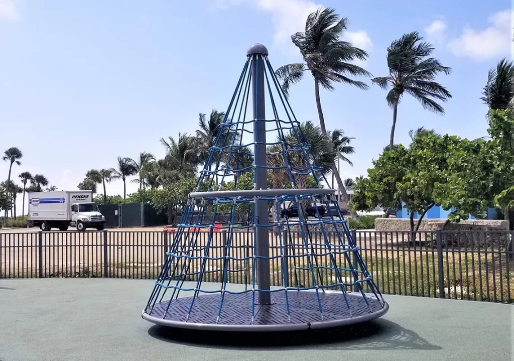 Apollo rotating climber with rope netting around a central pole shaped like a cone in a sunny park with palm trees