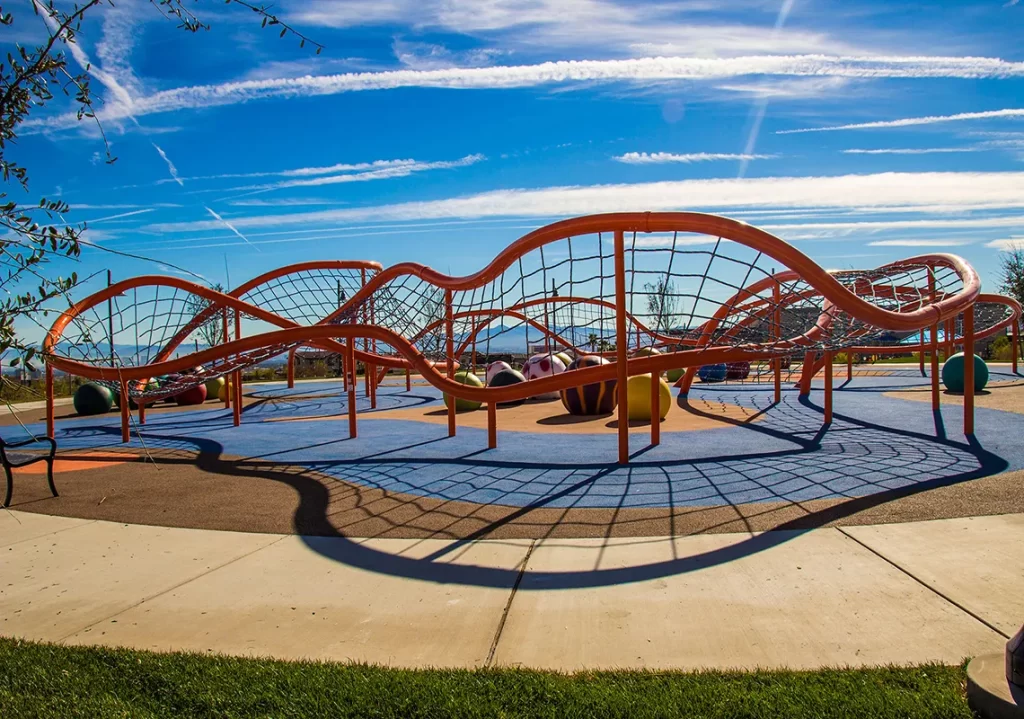 Wavy orange ropes course climbing structure with netting stretches across a colorful playground under a bright blue sky