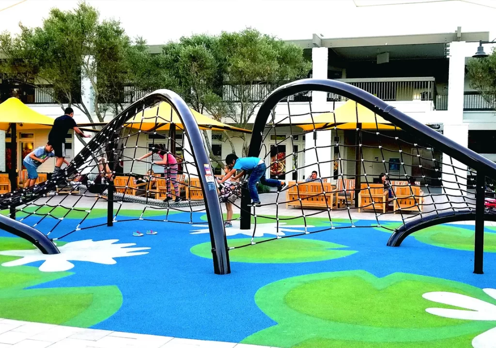 Kids climbing curved rope structures in colorful playground with seating area